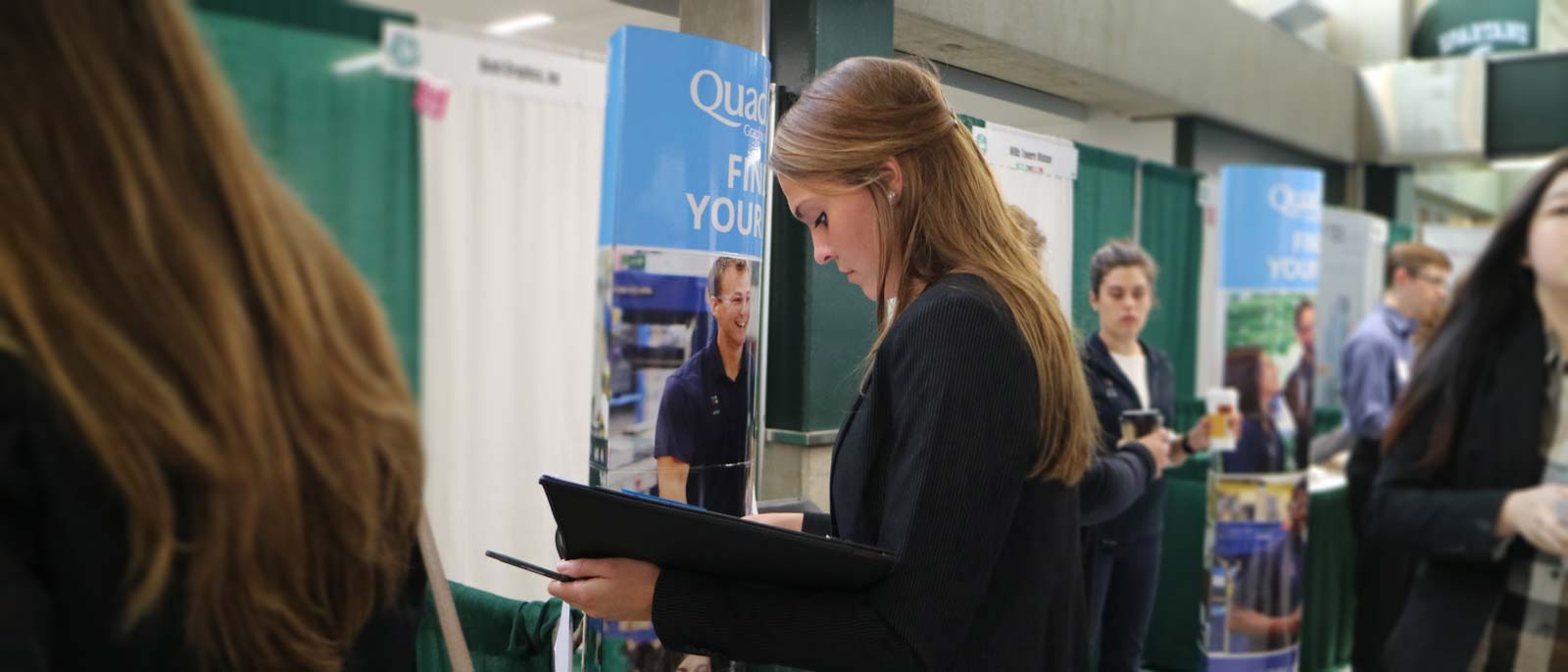 Female student dressed business professional looks down at a notebook while standing int eh concourse at the Breslin Student Events Center.