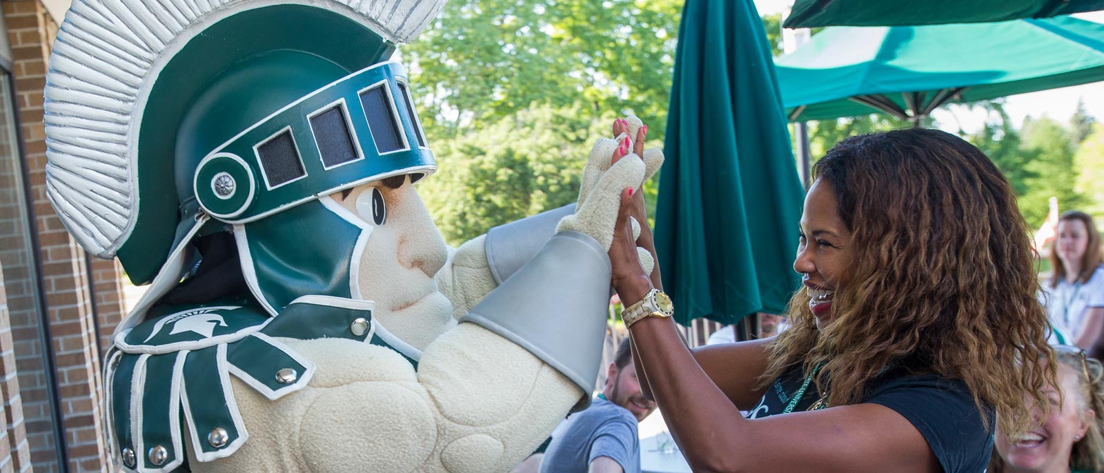 Woman high fives Sparty in an outdoor patio setting on a sunny day outside the Henry Center