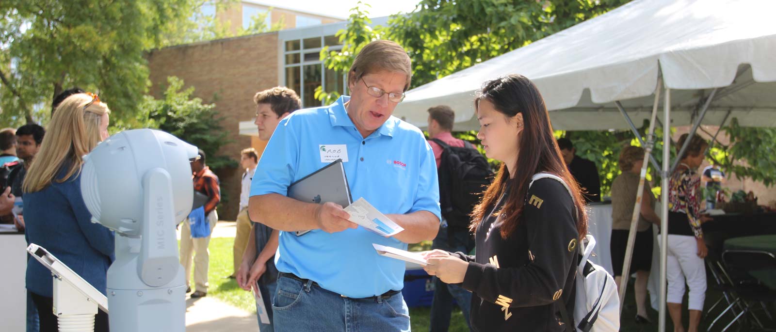 A male recruiter outside BCC shows information on a brochure to a female undergraduate student.