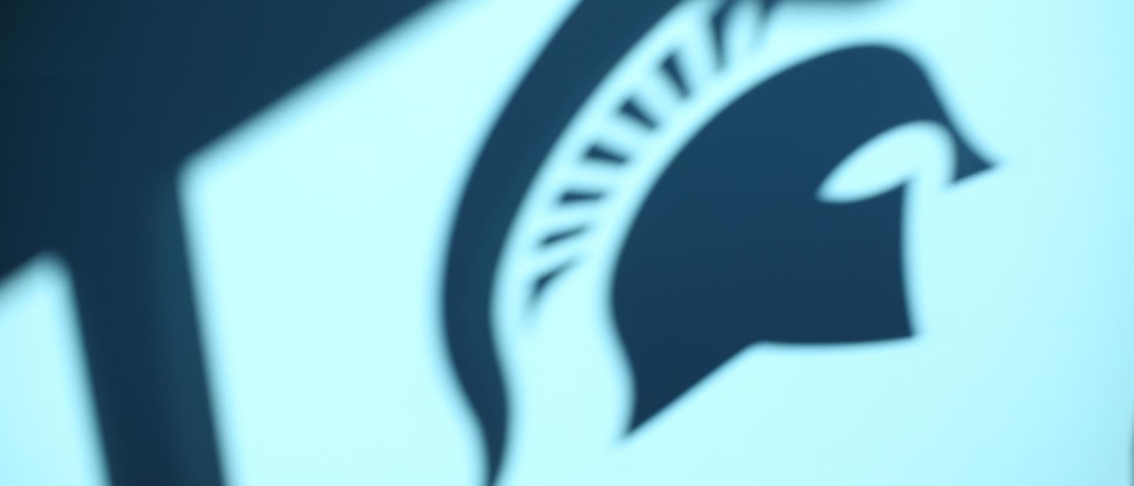 Silhouette of Spartan helmet logo against a lit wall