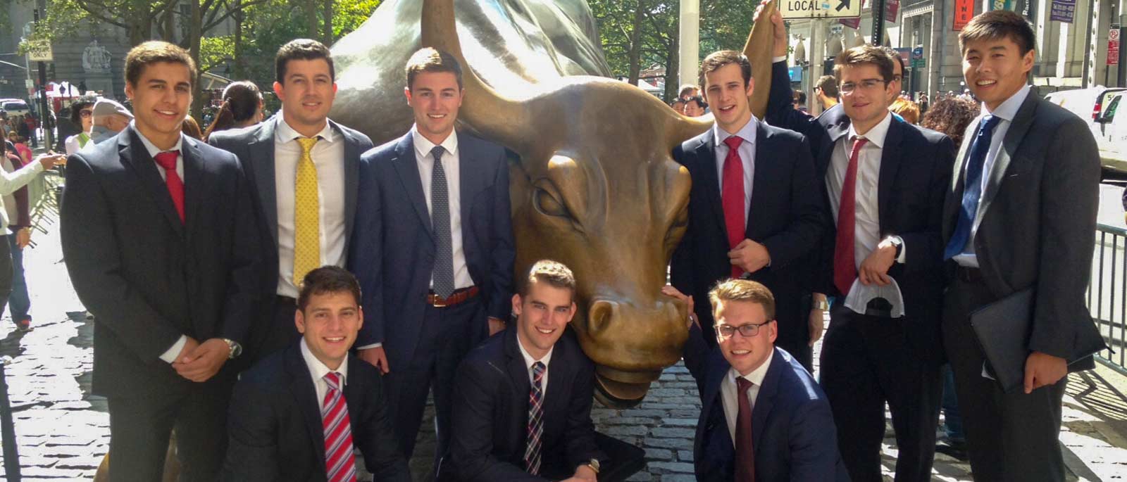 Group of FMI scholars in business professional attire gather around the Wall Street bull on a sunny day.