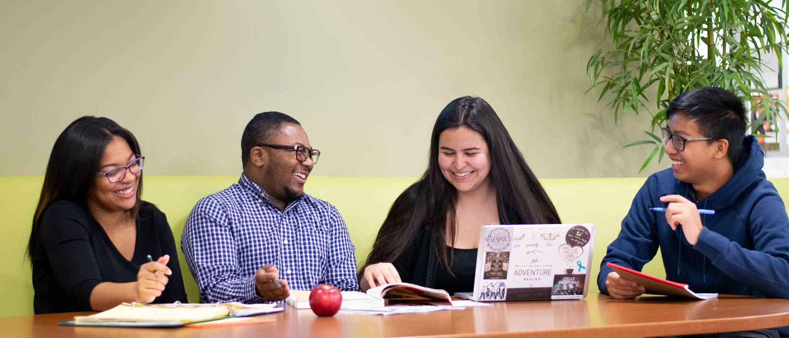 Four undergraduate students sit at a booth and smile as they study together.