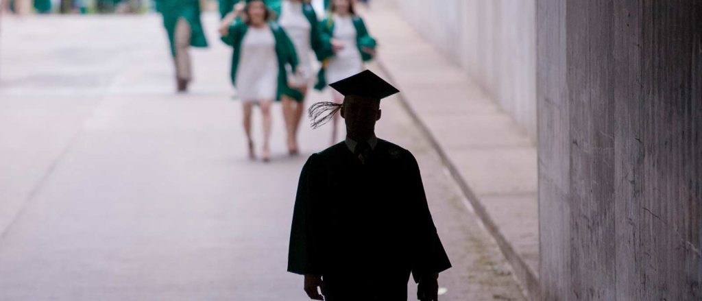 Silhouette of a student walking into the tunnel under the Breslin Center, wearing cap and gown.