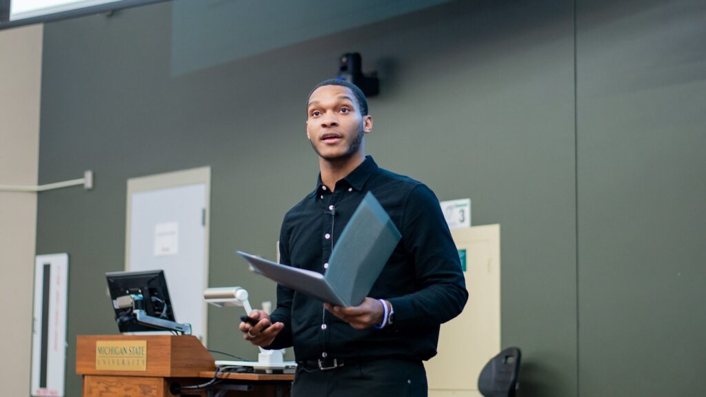 A student stands with a booklet giving a presentation in the Broad College.