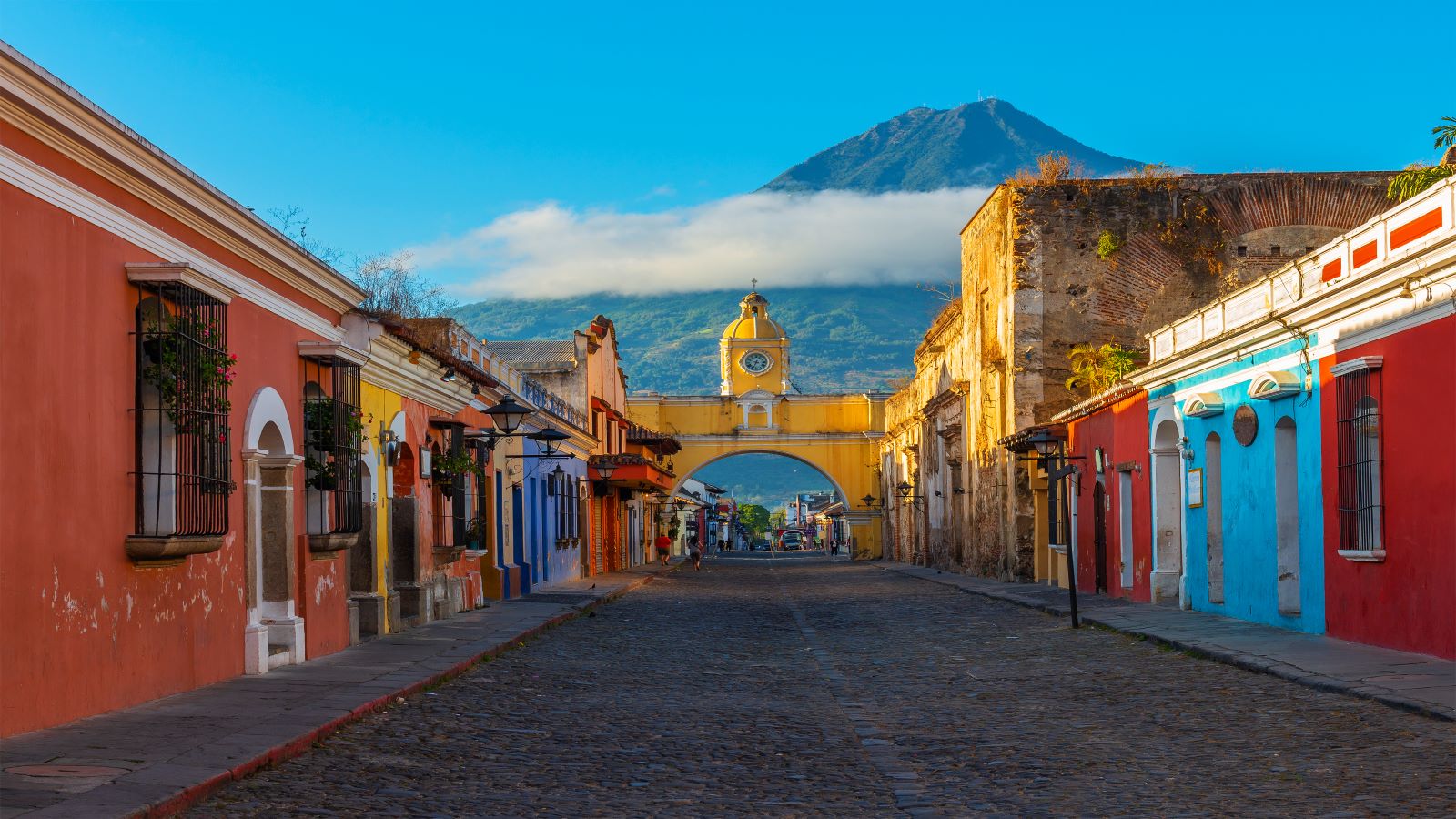 Cityscape of the main street and yellow Santa Catalina arch in the historic city center of Antigua at sunrise with the Agua volcano, Guatemala.