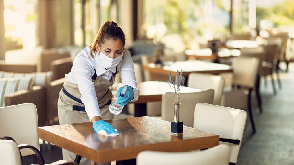 Waitress disinfecting tables wearing face mask and gloves.