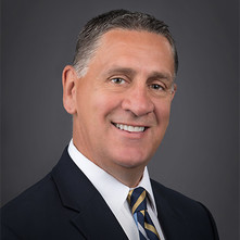 Headshot of man wearing suit and tie with grey background