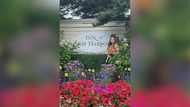 Sarah Lynch stands in front of Inn at Bay Harbor sign and behind a garden of flowers