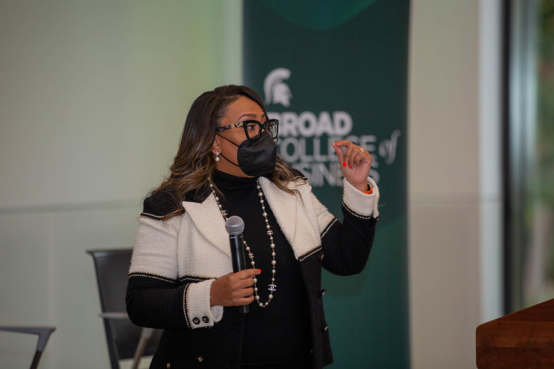 Broad alumna Dalana Brand holding a microphone speaking at a college-hosted event.