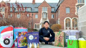Brendan Wang sits on the sidewalk on campus with various gift bags spread around him.