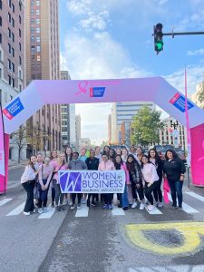 A group of women hold a Women in Business Students' Association banner under an inflatable awning for at a breast cancer walk in downtown Lansing.