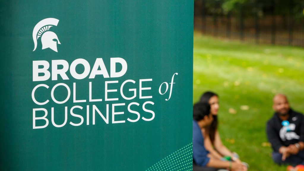 Broad College of Business banner outside on MSU's campus in front of students sitting on the lawn