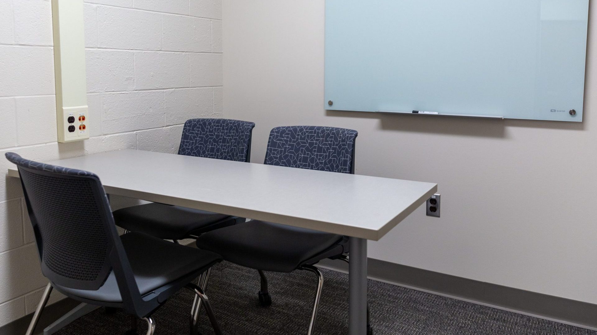 Broad behavioral lab seating area with a whiteboard, three chairs and a table.
