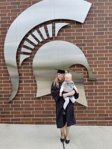 Bianca Bouchonnet wearing cap and gown for graduation while holding her daughter.
