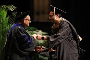 An Executive MBA student crosses the stage at graduation and fist bumps Dean Sanjay Gupta.