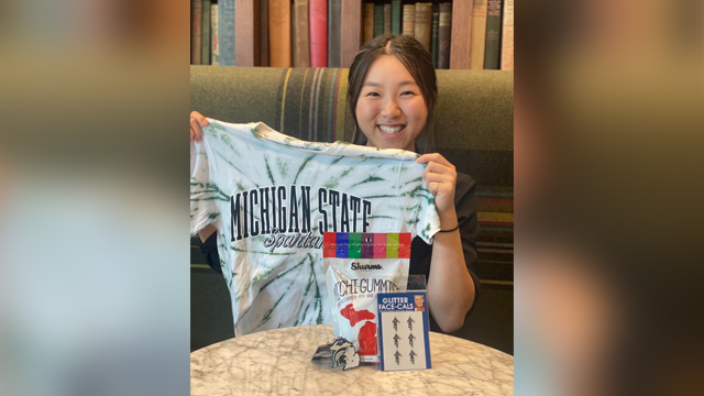 Alice Kim smiling holding a Michigan State t-shirt for the camera