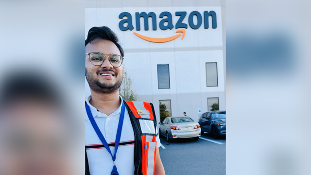 Dilavar Goyal posing in front of Amazon Warehouse logo wearing an Orange Safety Vest