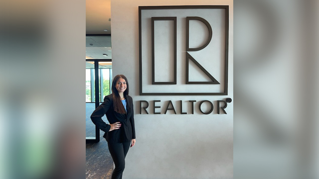 Angelina Baglio standing in front of a wall with the Michigan Realtors logo