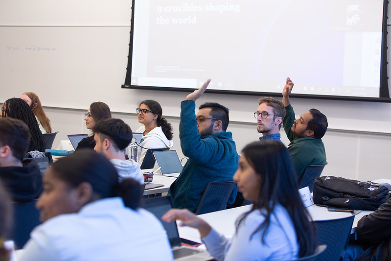 MBA students seated in classroom, raising hands.