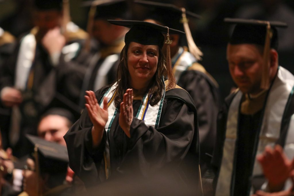 A woman stands and claps her hands, dressed in cap and gown at the Executive MBA commencement ceremony.