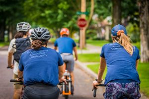 People ride bicylces away from the camera, wearing matching tshirts about the Groundwork Center's mission.