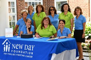 New Day Foundation for Families nonprofit staff wear matching, branded polo shirts, pose behind a table with a New Day blue tablecloth.