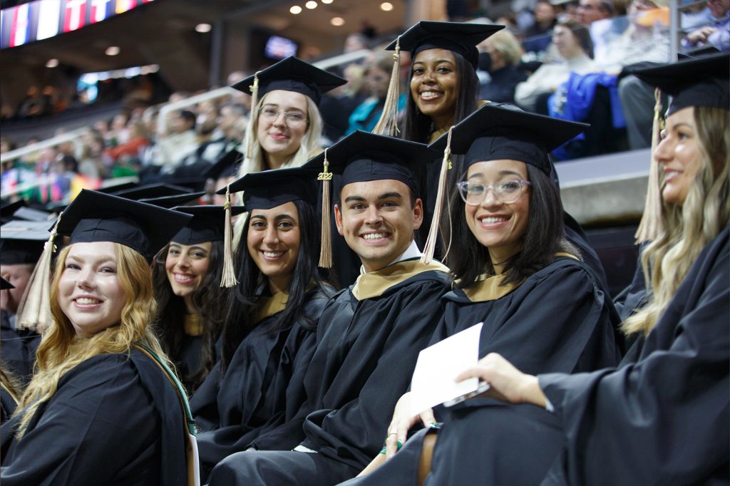 Class of 2022 Broad master's graduates smile for a picture while seated in the Breslin Center bleachers at commencement.