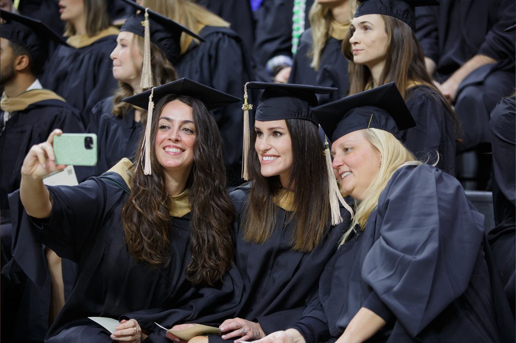 Advanced degree graduates from the Class of 2022 take a selfie while seated in the Breslin Center bleachers at commencement.