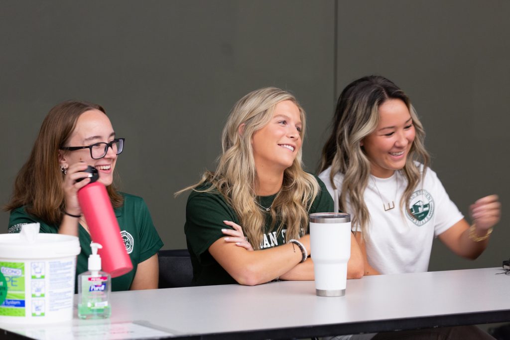 Three female students smile and sit at a table.