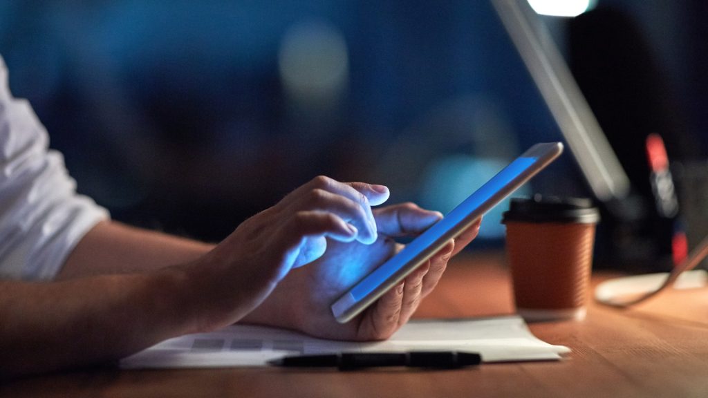 Cropped image of someone using a tablet at a desk at night.
