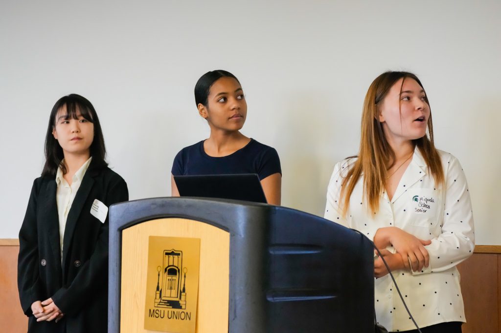 Layna Cho, Lauryn Davis and Miquela Ochoa give a group presentation at a podium with MSU Union branding on it.