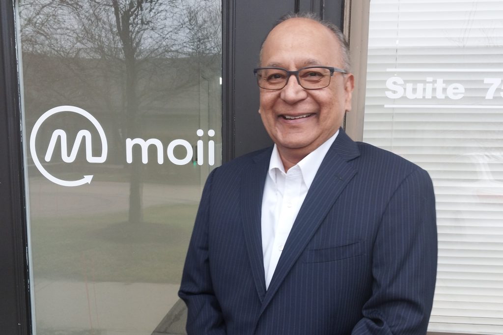 Madhu Posani stands in front of a glass door with the Moii logo on it.