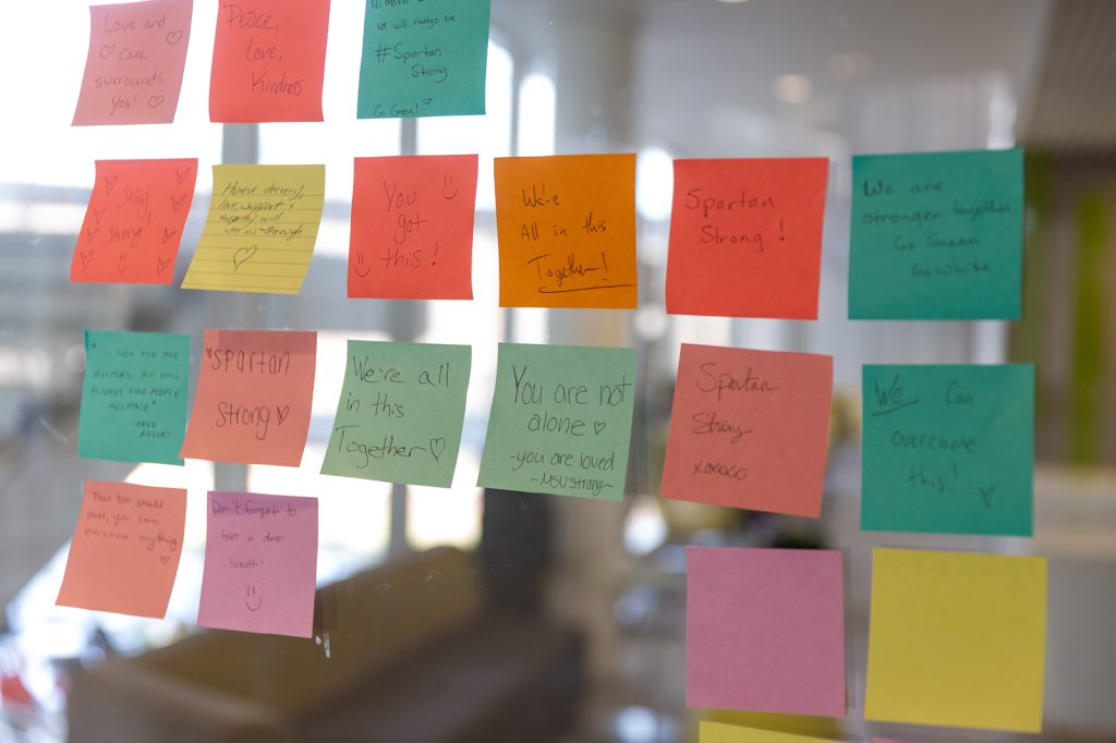 Multiple sticky notes on a glass wall offer positive, supportive messages for the MSU community.