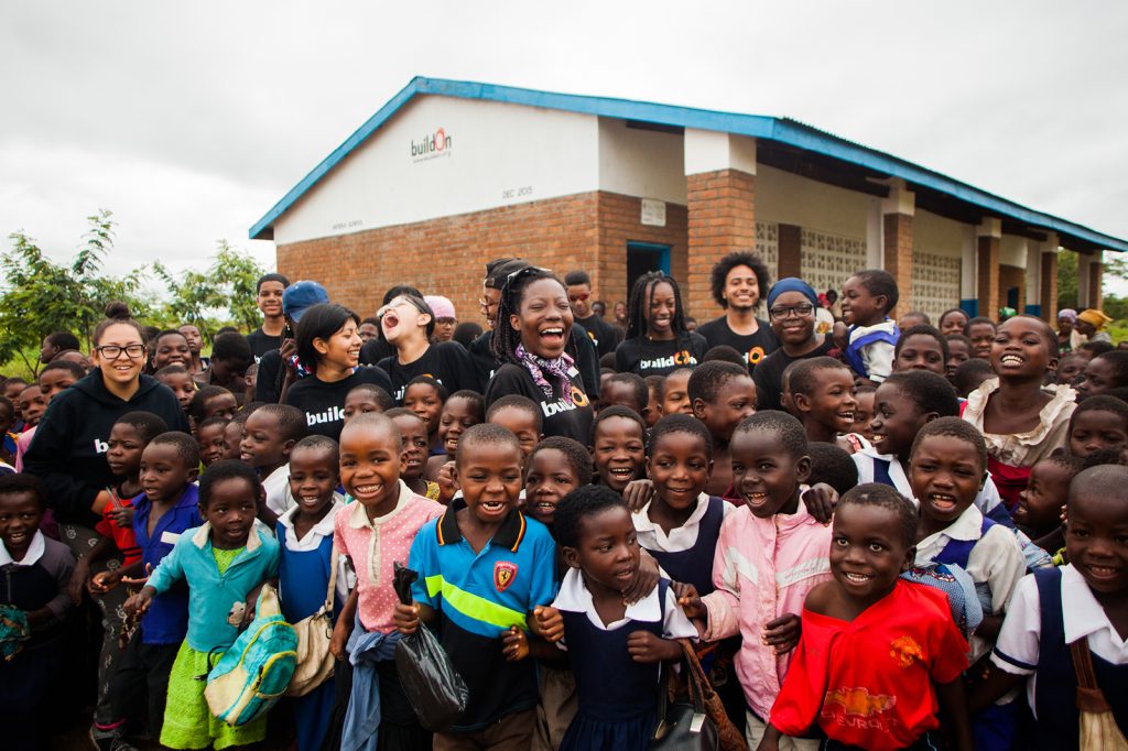 A group of buildOn volunteers and students pose for a picture outside a school building they constructed.