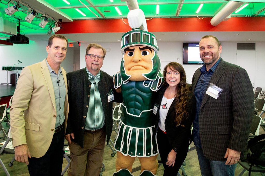 Alumni, staff and friends, including Larry Bell, pose with MSU mascot, Sparty, at the MSU Detroit Executive Forum in 2018.