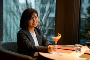 Kaori Koide holds a mocktail glass while seated at a professional networking event.