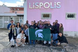 Broad MBA students pose with a Spartan flag in front of Lispolis while on study abroad in Portugal.