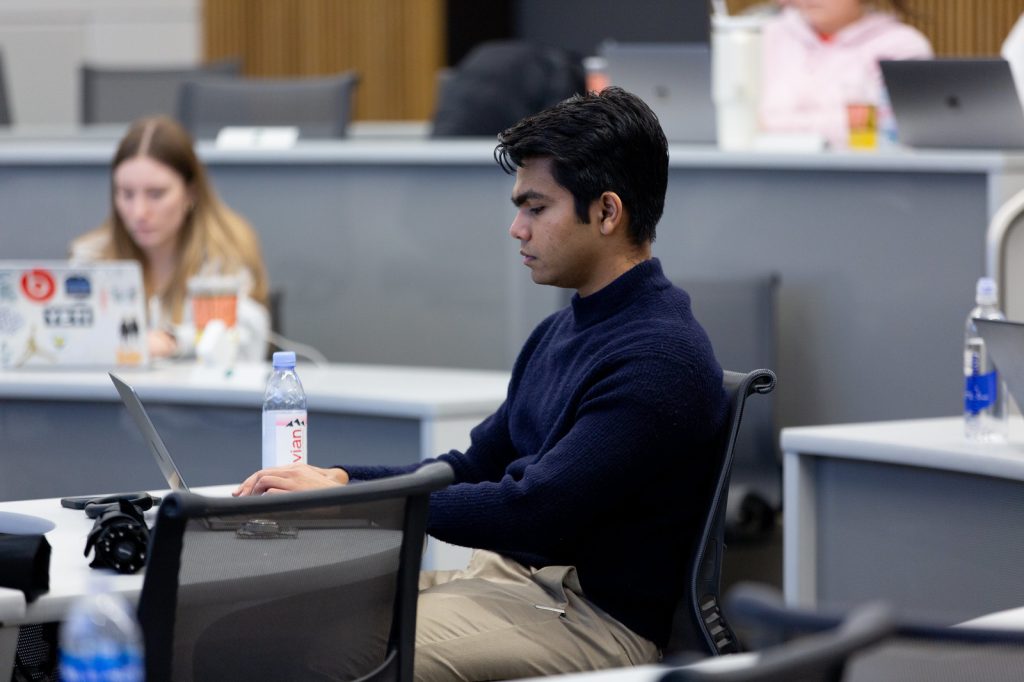 Close up of a student typing on a laptop while seated in a classroom in the Minskoff Pavilion.