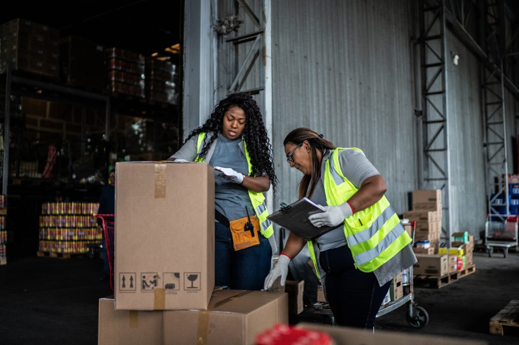 Two warehouse workers checking boxes to process and deliver.