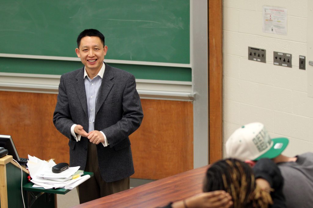 John Jiang stands in front of a chalkboard while teaching an accounting course.