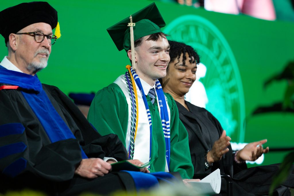 Carlos Conrad and other platform party members seated on stage, smiling during the Broad College 2023 commencement ceremony.