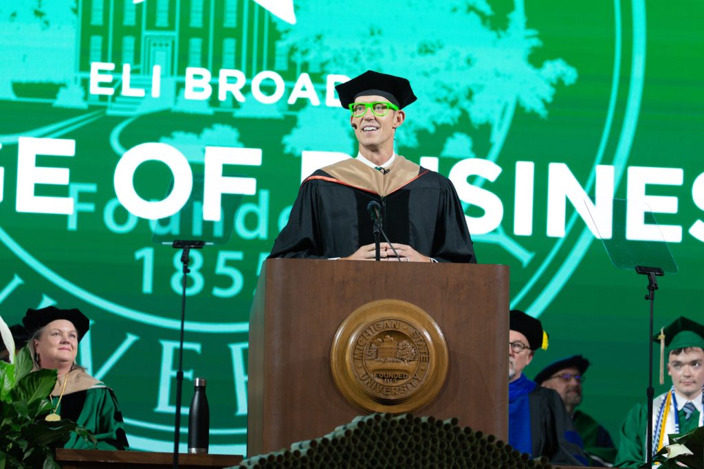 Erik Qualman in academic regalia speaking from the podium at Breslin Center for the Broad College's 2023 commencement ceremony.