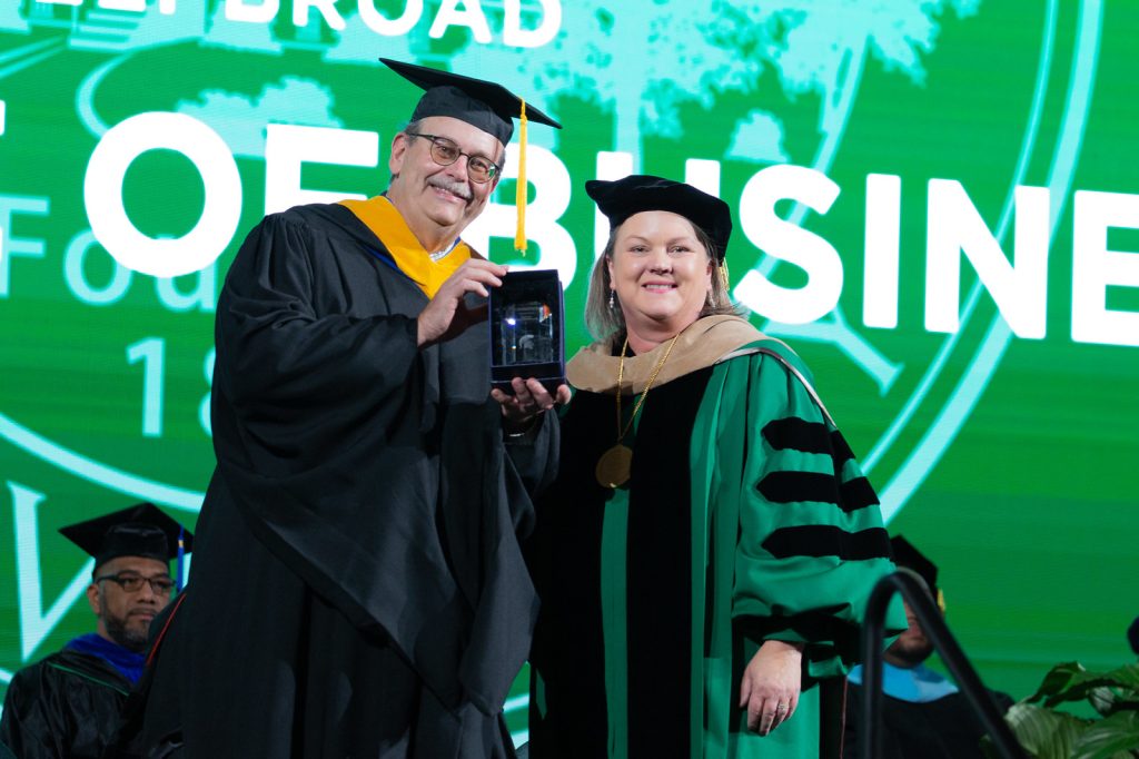 Jerry Jonckheere and Interim Dean Judith Whipple stand on stage at the Breslin Center. Jonckheere received the college's Outstanding Alumni Achievement Award and holds it in the picture.