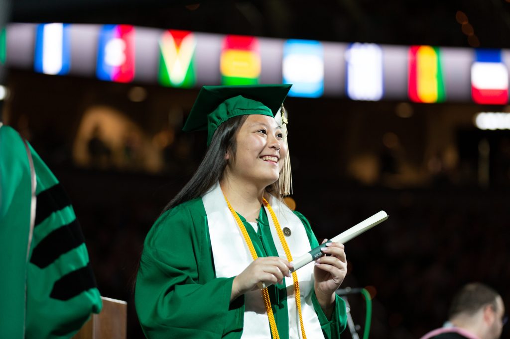 A woman holds her diploma after crossing the Breslin Center stage at commencement.
