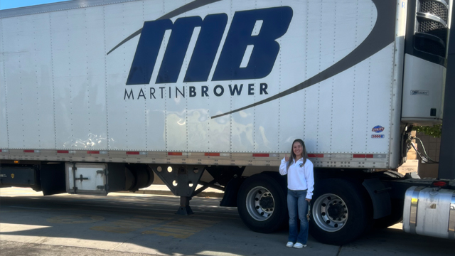 Emily Goodman smiling and holding a thumbs up in front of a Martin Brower truck