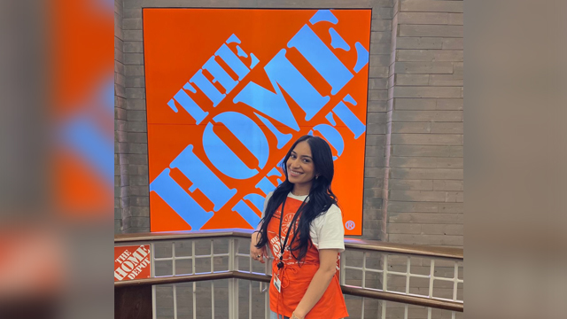 Sumaiya Asghar wearing a Home Depot apron posing in front the The Home Depot sign