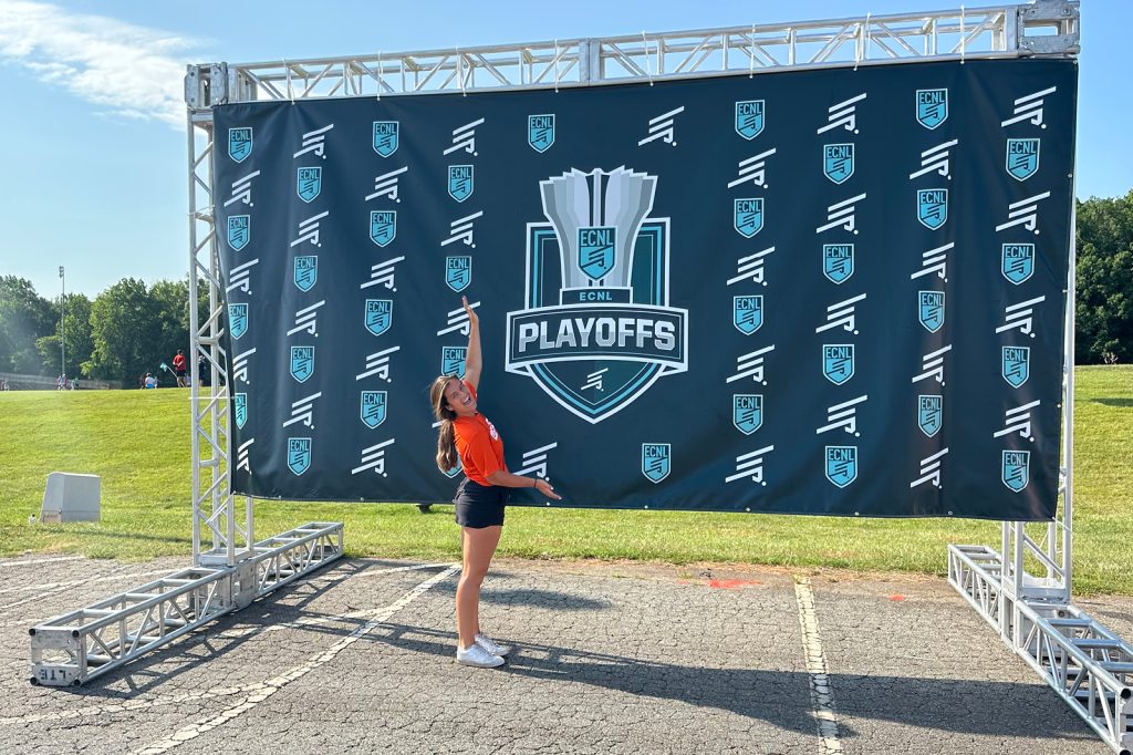 Anna Malmquist poses in front of a ECNL Playoffs banner during her sports business management internship.