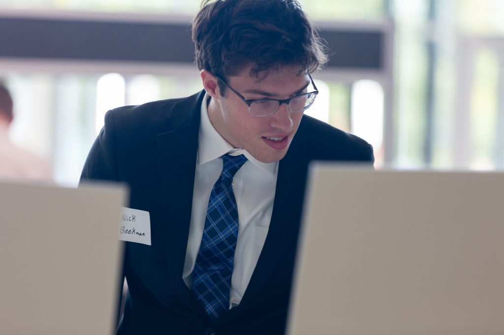 A Spartan dressed in business professional clothing reads poster boards at a career fair.