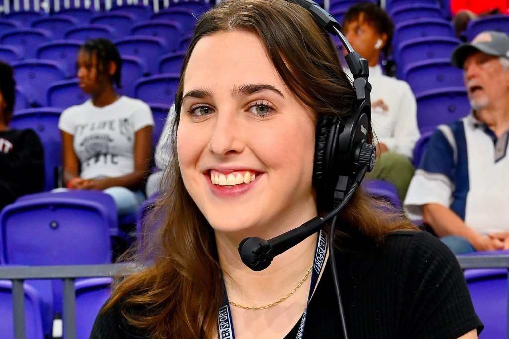 Julie Hopp at wearing a headset on the sidelines during a college basketball game.