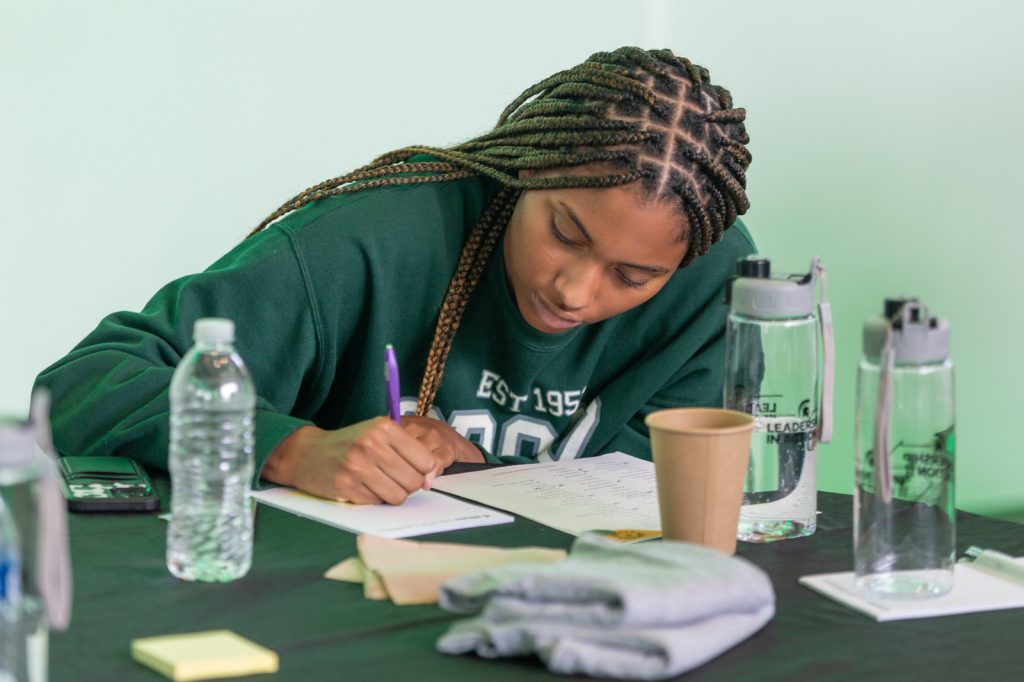 A Spartan wears a Broad College sweatshirt and takes notes.